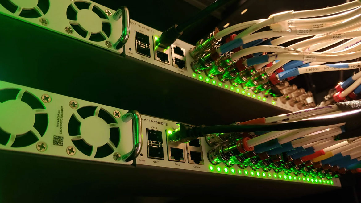 Two NVT PHYBRIDGE network switches with numerous cables plugged into ports, illuminating with green indicator lights.