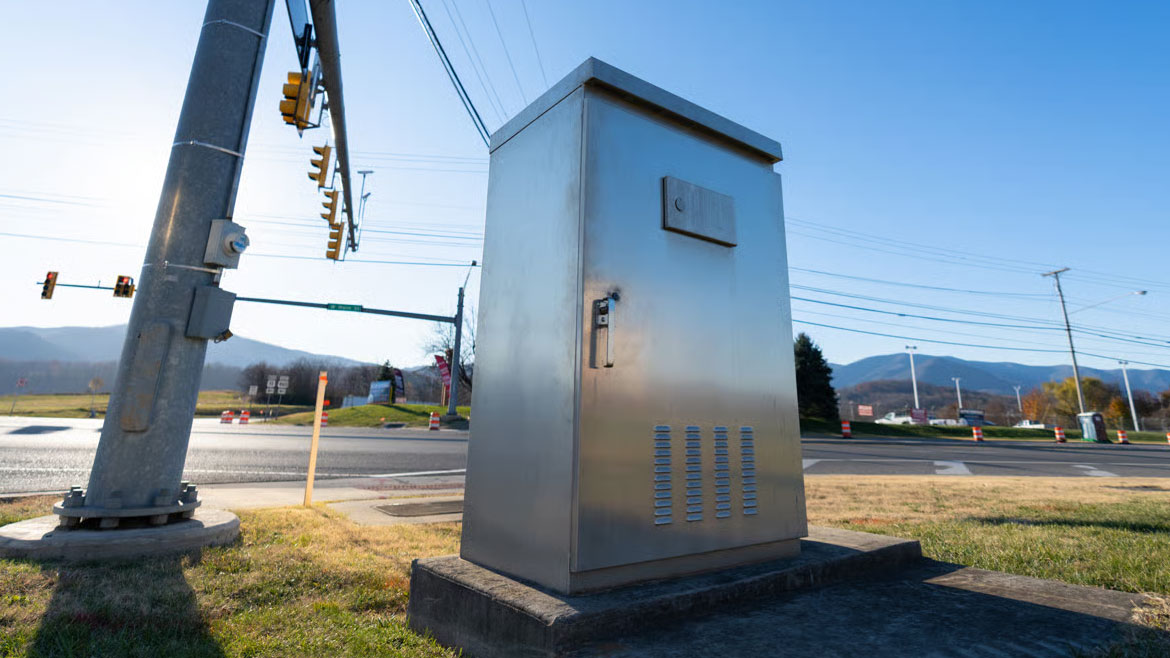 A metal utility box and a traffic light pole at a rural intersection under a clear blue sky.